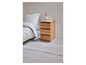 Een houten nachtkastje met drie laden naast een wit bed.