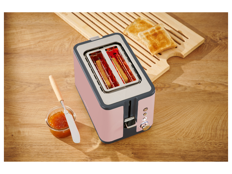 Een roze broodrooster met twee sneetjes toast op een houten plank.