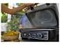 Personne ouvrant un multicuiseur avec des épis de maïs à proximité, montrant les fonctions grill et friteuse à air.