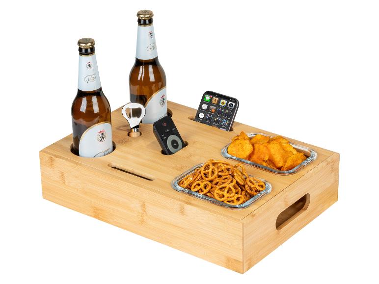Plateau de service en bambou avec bouteilles de bière, snacks, ouvre-bouteille, télécommande et téléphone.