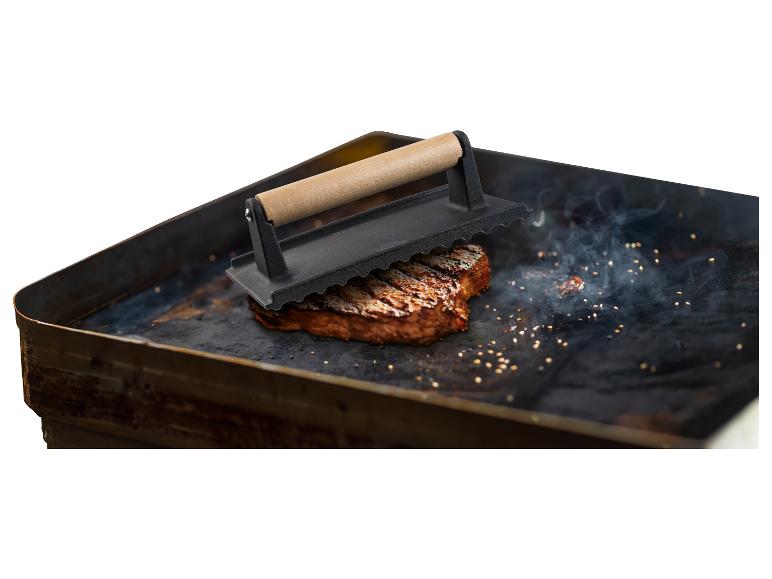 Gebakken biefstuk op een grillplaat met steakpers.