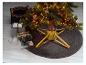 Een verlichte kerstboom met ballen staat op een rond vloerkleed, omringd door cadeaus.