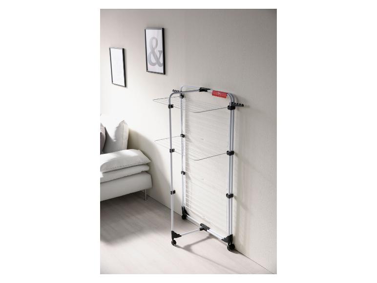 Verticaal droogrek met wielen in een woonkamer met een bank en schilderijen.