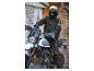 Een motorrijder op een witte Ducati Scrambler met zwarte kleding en een helm.