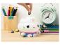 Main plaçant une pièce dans une tirelire chat-cupcake, avec des fournitures scolaires autour.