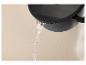 Water dat uit een zwarte pan met deksel stroomt tegen een beige achtergrond.
