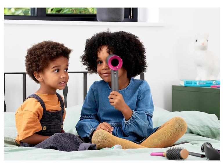 Twee kinderen spelen met een Dyson föhn en borstels.