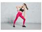 Une femme en leggings roses et un soutien-gorge de sport noir s'entraîne avec un kettlebell rose.