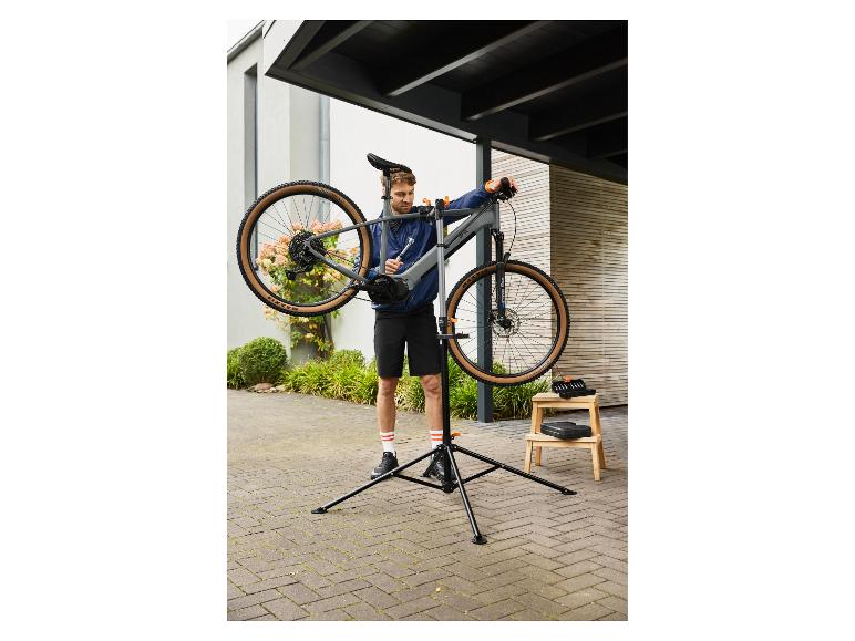 Homme réparant un vélo sur un support de réparation de vélo en extérieur.