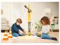 Deux enfants jouent avec une grande grue jouet et des cacahuètes d'emballage sur un tapis.