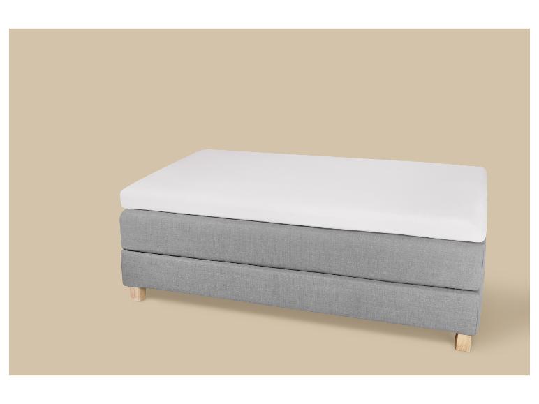 Eenpersoonsbed met wit matras en grijze stoffen onderbouw met houten poten.