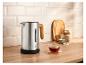 Bouilloire en acier inoxydable avec poignée en bois, une tasse de thé et accessoires sur un comptoir en bois.