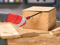 Een hand met een rode handschoen opent een houten doos met een breekijzer.