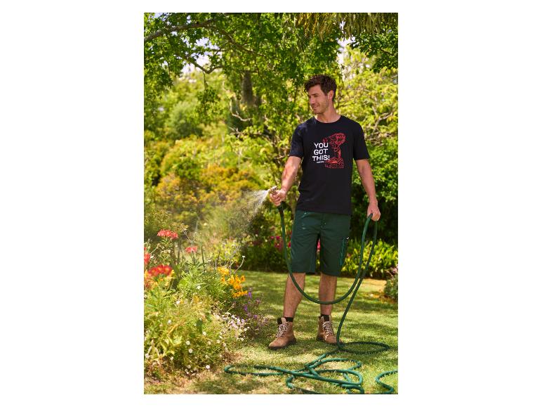 Homme arrosant des fleurs dans un jardin, portant un t-shirt noir 'YOU GOT THIS!' et un short vert.