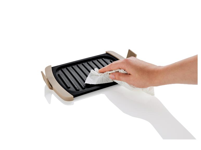 Une main nettoie une plaque de cuisson avec une serviette en papier.