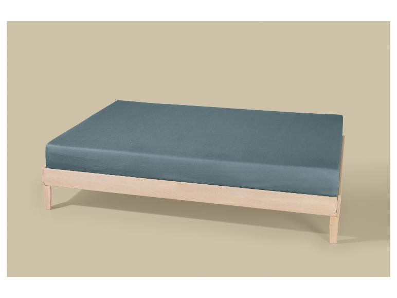 Cadre de lit en bois clair avec un matelas bleu-gris sur fond beige.
