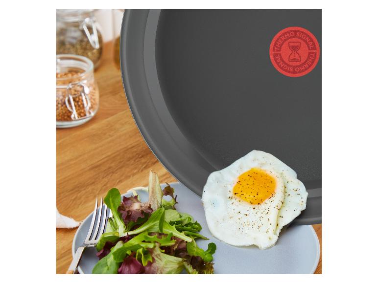 Tefal koekenpan met gebakken ei en salade op een bord, kruiden op de achtergrond.