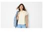 Femme en t-shirt brodé, pantalon bleu et veste en jean sur l'épaule.