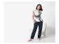 Femme souriante en t-shirt rayé et pantalon bleu foncé, pieds nus, à côté d'une chaise blanche.