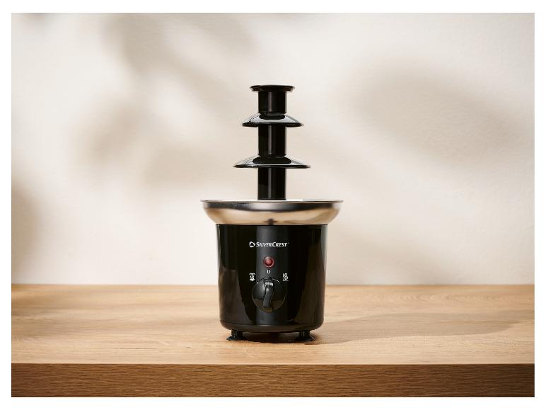 Een zwarte drielaagse chocoladefontein met een roestvrijstalen basis, op een houten tafel.