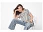 Femme en t-shirt rayé et jean assise sur une chaise blanche.