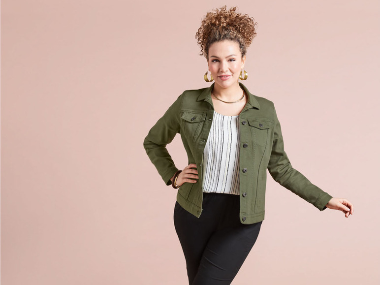 Een vrouw draagt een groene denimjas met een gestreept shirt en zwarte broek.