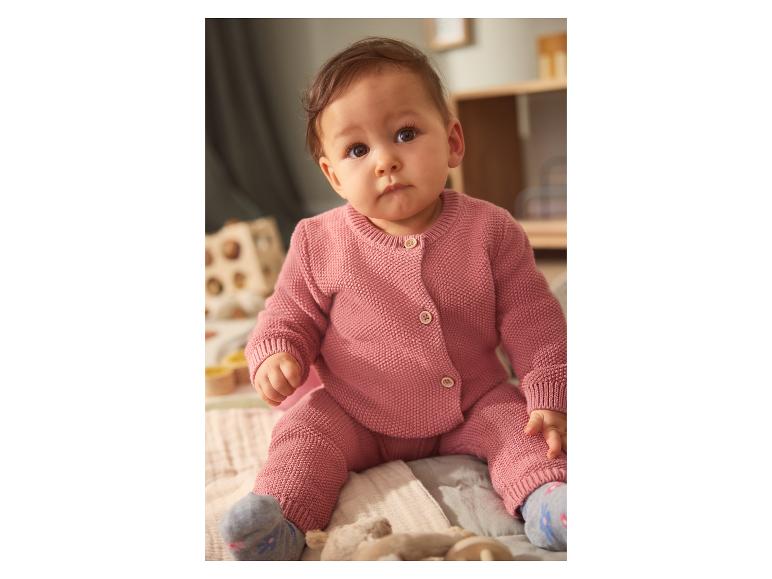 Bébé en ensemble tricoté rose, assis sur une couverture douce.