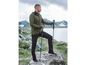 Homme en veste verte et pantalon noir avec des bâtons de randonnée dans un paysage montagneux.