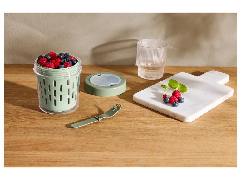 Récipient à collation avec myrtilles, framboises et groseilles, à côté d'une fourchette pliable et d'une planche de fruits.