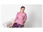 Vrouw in roze pyjamatop met lange mouwen en geruite broek zit op een stoel.