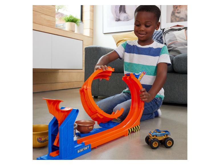 Un garçon souriant joue avec un circuit Hot Wheels Monster Trucks et une voiture.