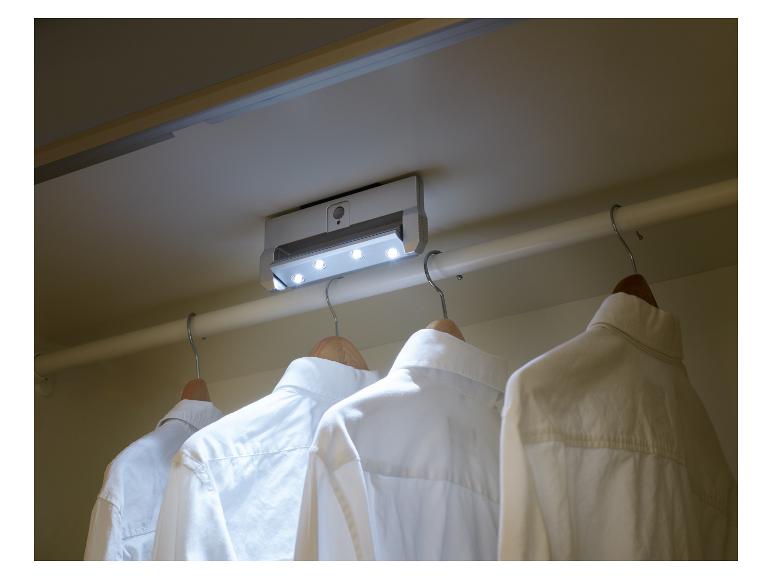 Witte overhemden hangen aan een kapstok in een kast verlicht door een plafondlamp.
