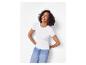 Lachende vrouw in een wit T-shirt en jeans, leunend tegen een muur.