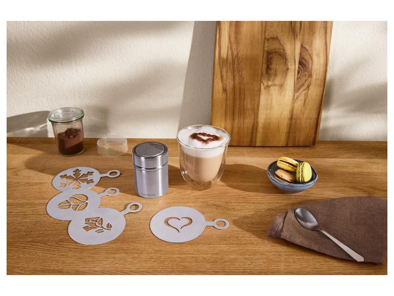 Koffiesjablonen en cacaostrooier met een latte en macarons op een houten tafel.