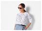 Femme en pull en maille blanc, jupe en jean et lunettes de soleil.