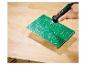 Main soudant une carte de circuit imprimé verte sur un établi en bois.
