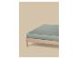 Een lichtgroen hoeslaken op een houten bedframe tegen een beige achtergrond.