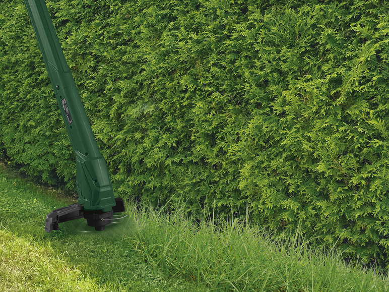 Une débroussailleuse verte taille de l'herbe le long d'une haie.