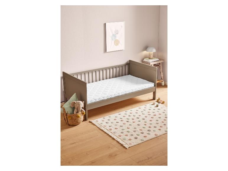 Een babybed met een wit dekbed en een vloerkleed met stippen.