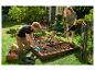 Deux personnes jardinent, plantant des semis dans un potager surélevé avec des outils de jardinage.