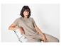 Vrouw in beige blouse en broek, zittend op een stoel.