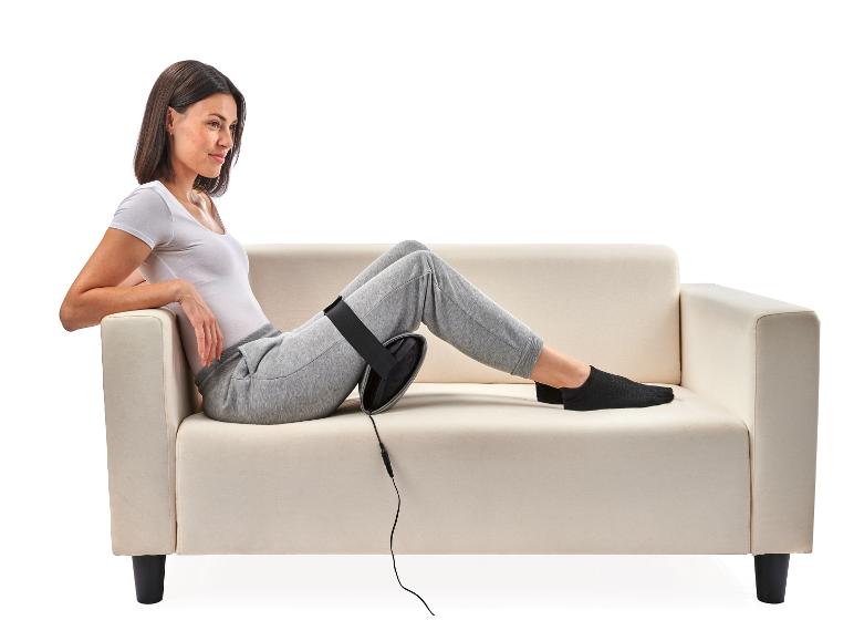 Une femme assise sur un canapé blanc avec un coussin de massage sur sa jambe.