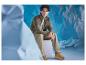 Homme en veste marron et pantalon kaki, assis sur un cube blanc.
