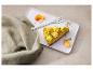 Een stuk cheesecake met mangoglazuur, slagroom, pistachenoten en kumquats op een wit bord.