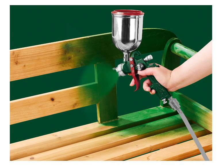 Une main utilisant un pistolet pulvérisateur pour peindre un banc en bois.