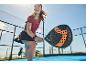 Femme en jupe et t-shirt jouant au padel avec une raquette en extérieur.