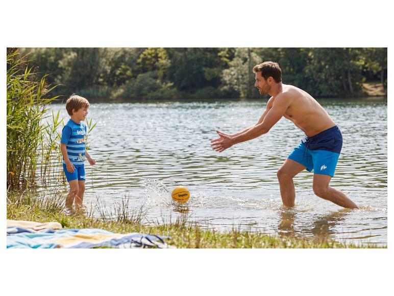 Père et fils jouent avec un ballon dans l'eau, portant des maillots de bain.