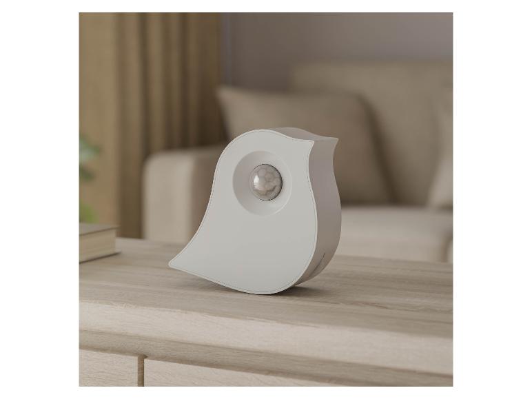Witte vogelvormige bewegingssensor op een houten tafel in een woonkamer.