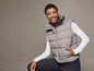 Een vrouw draagt een grijze puffer vest en een witte trui.