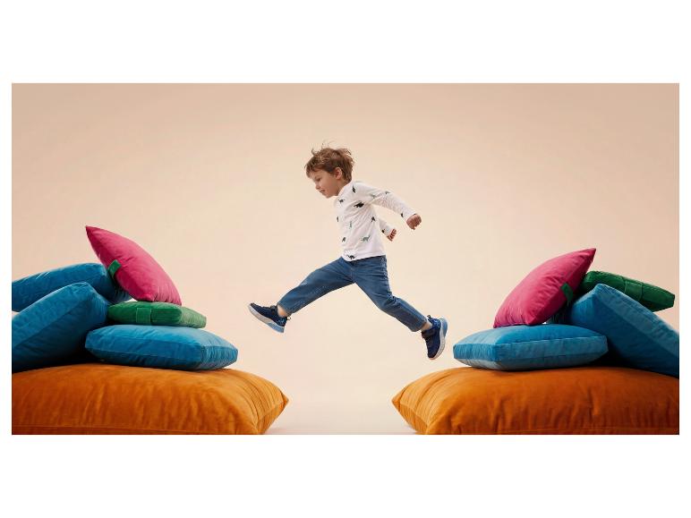 Enfant sautant entre des coussins colorés, portant un t-shirt dinosaure et un jean.